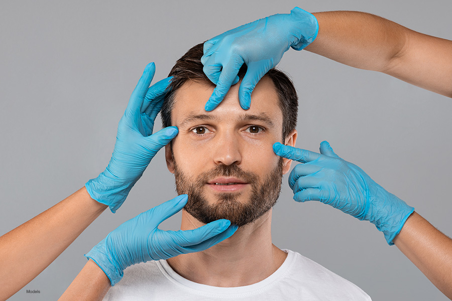 Doctors hands in protective medical gloves touching middle-aged man face over grey studio background.